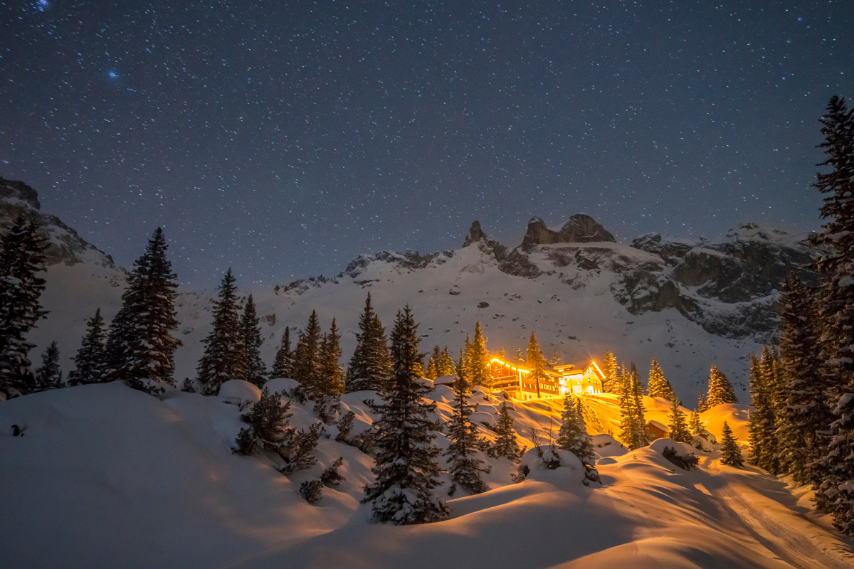 Lichtverschmutzung einer Berghütte in den Alpen bei Nacht im Winter.