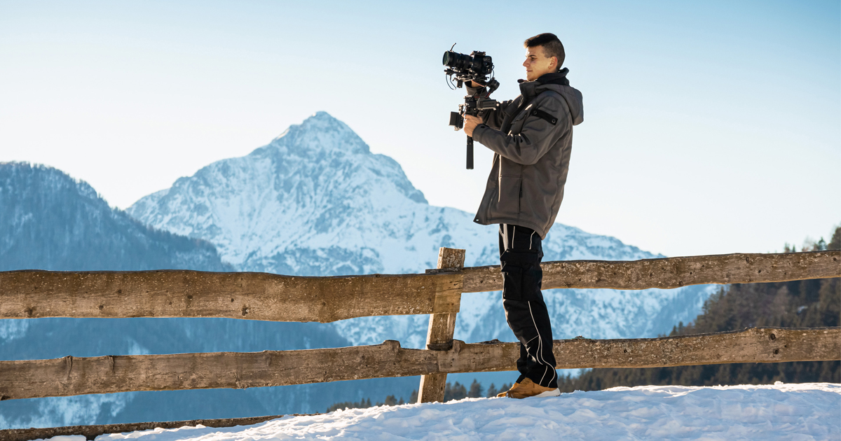 Junger Mann mit Filmkamera in einer verschneiten Berglandschaft.